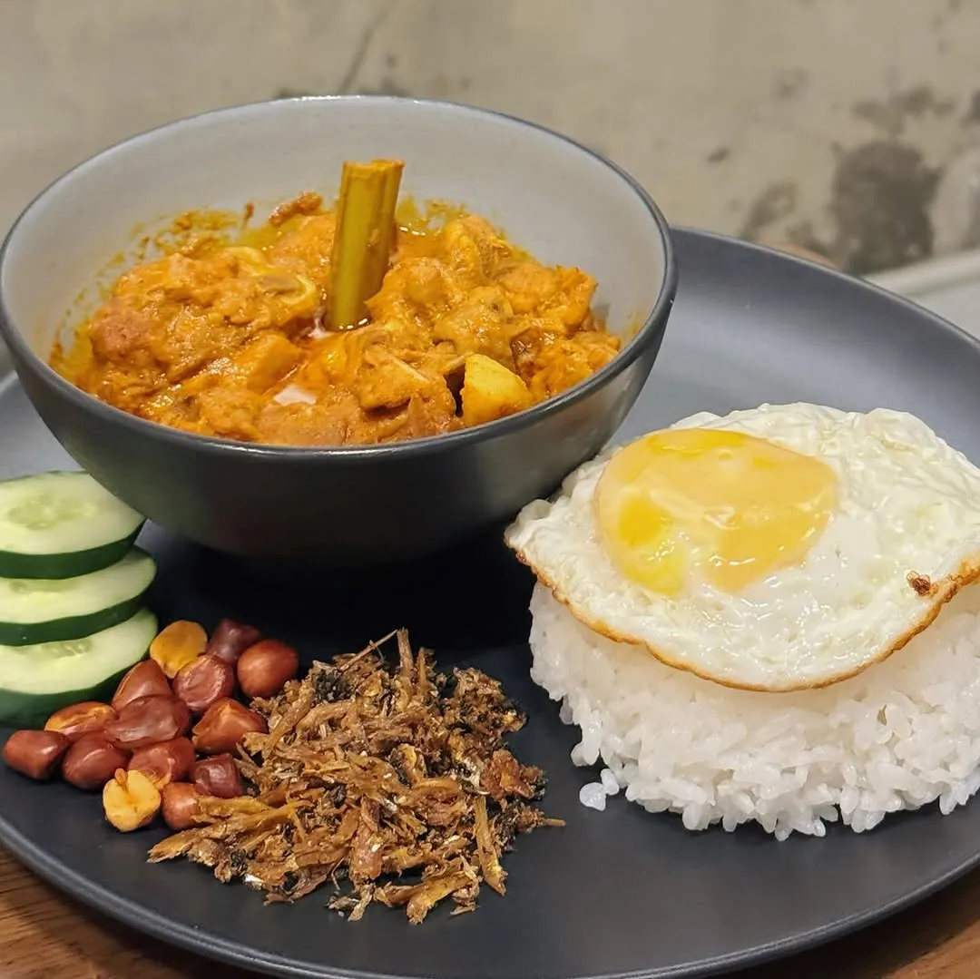 Nasi lemak plate featuring curry chicken, fried egg, cucumber, and peanuts.