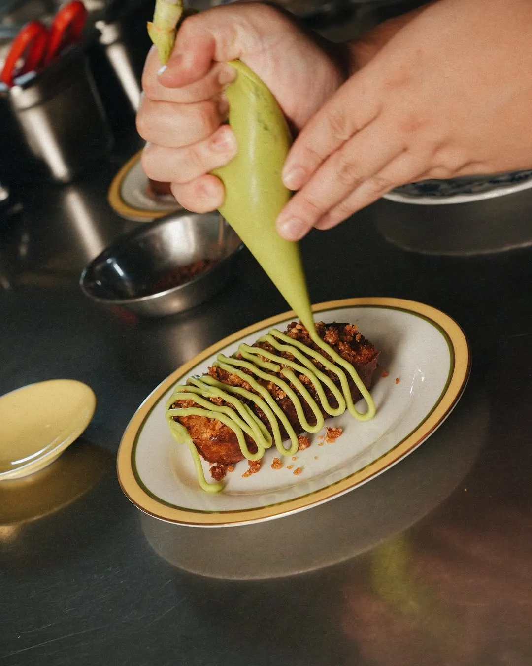 Decorative dessert being piped with green icing on a plate.
