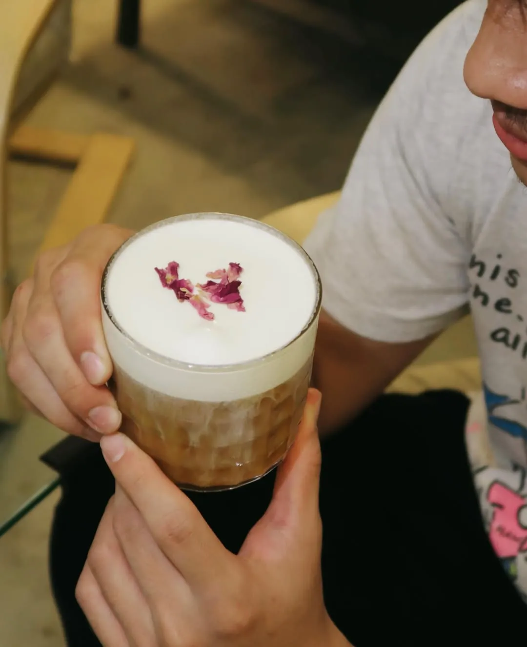 A hand holding a glass of creamy vanilla cloud cold brew topped with dried rose petals.