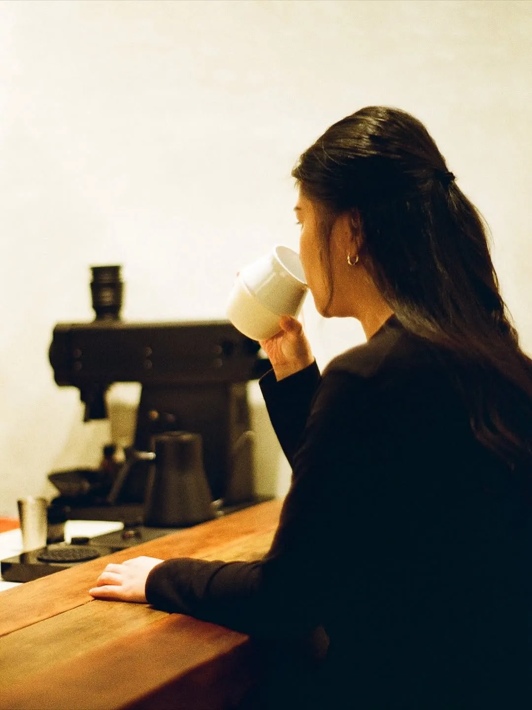 A person savoring coffee at a cafe counter with a brewing machine.