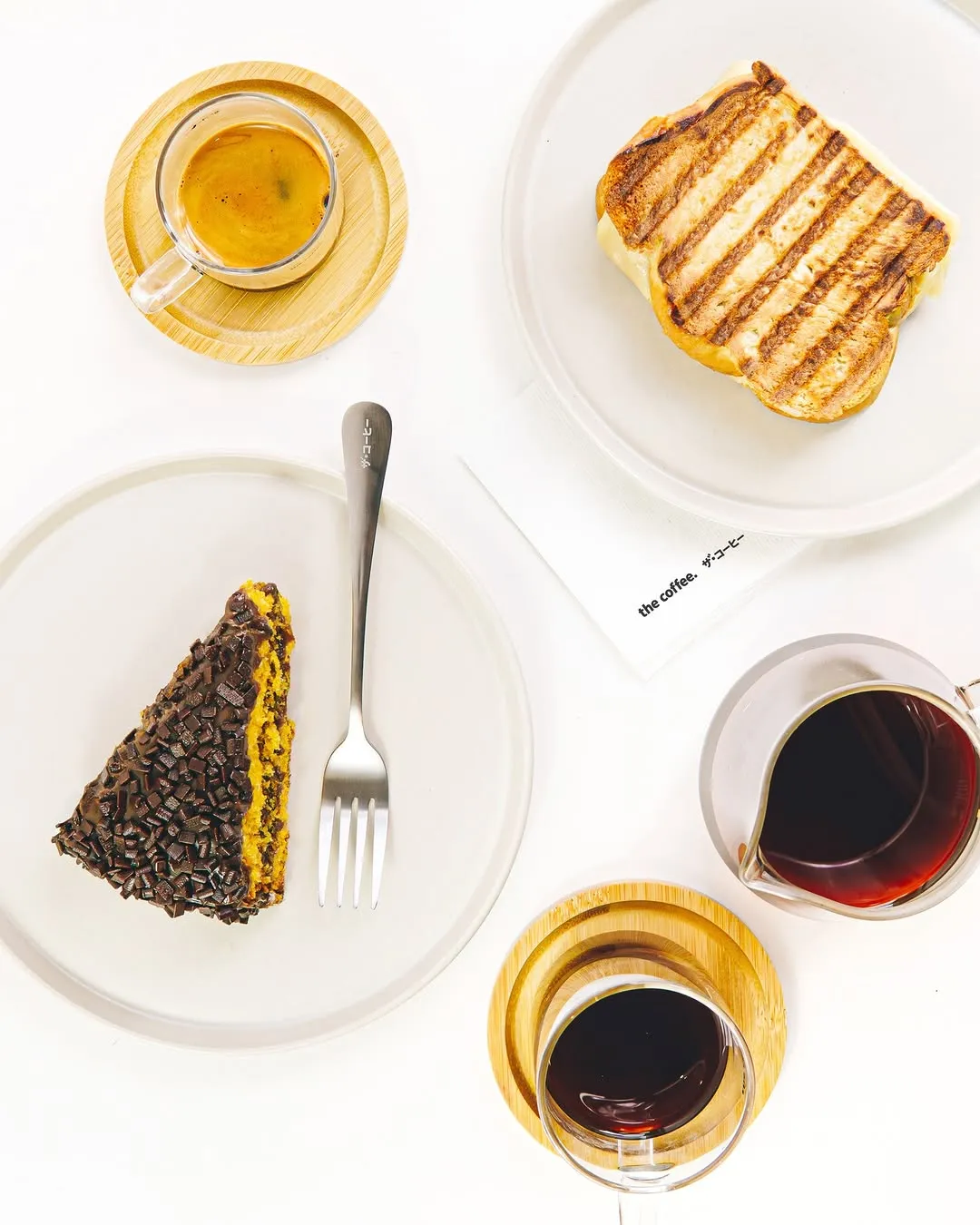 Carrot cake slice, grilled sandwich, and fresh coffee on white plates.