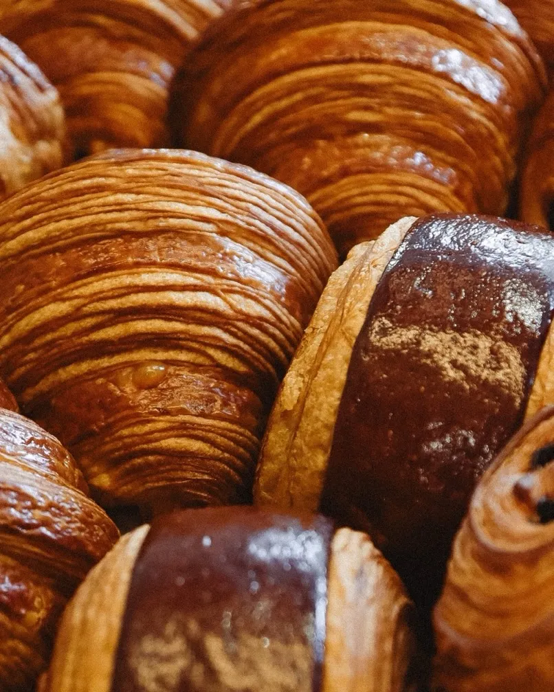 Close-up of golden-brown croissants and chocolate pastries piled together.