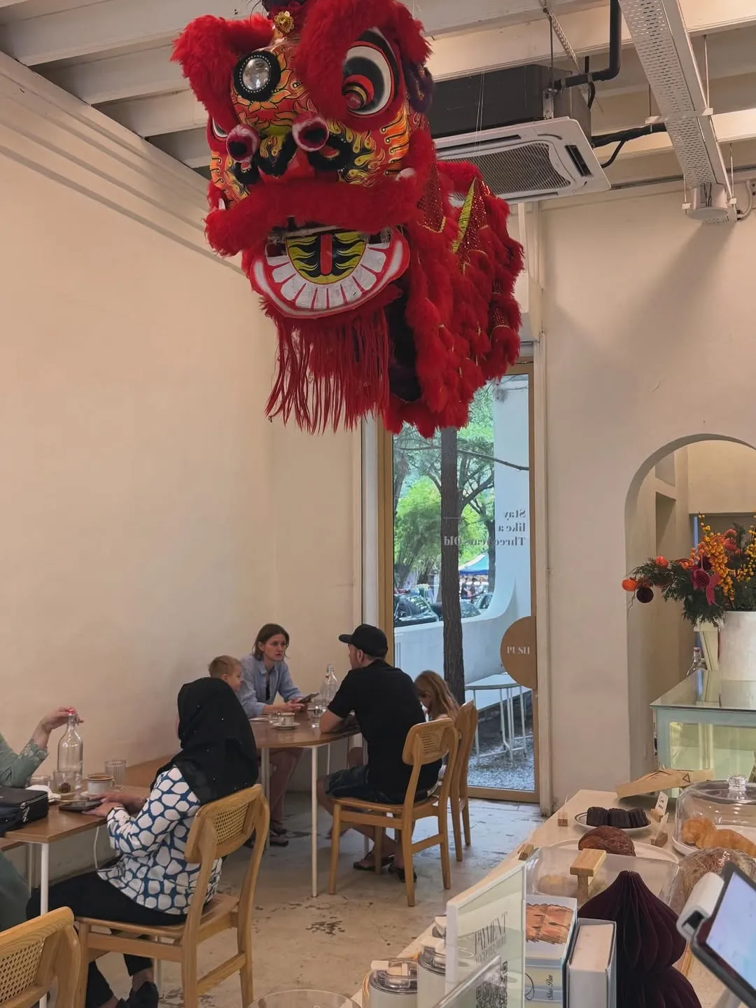 Lion dance decoration hanging above tables in a lively cafe atmosphere.