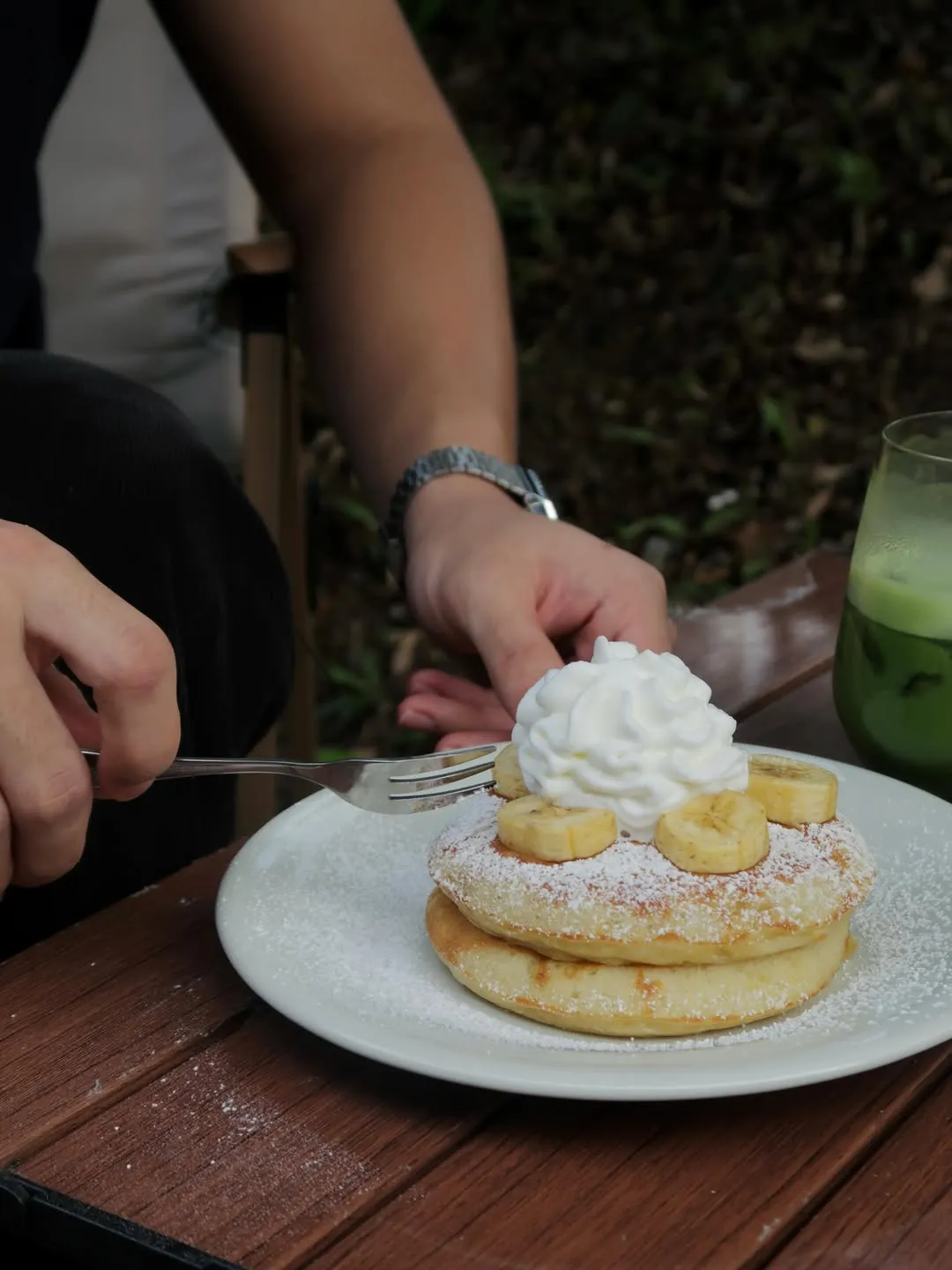Close-up of banana pancakes with powdered sugar, whipped cream, and banana slices.