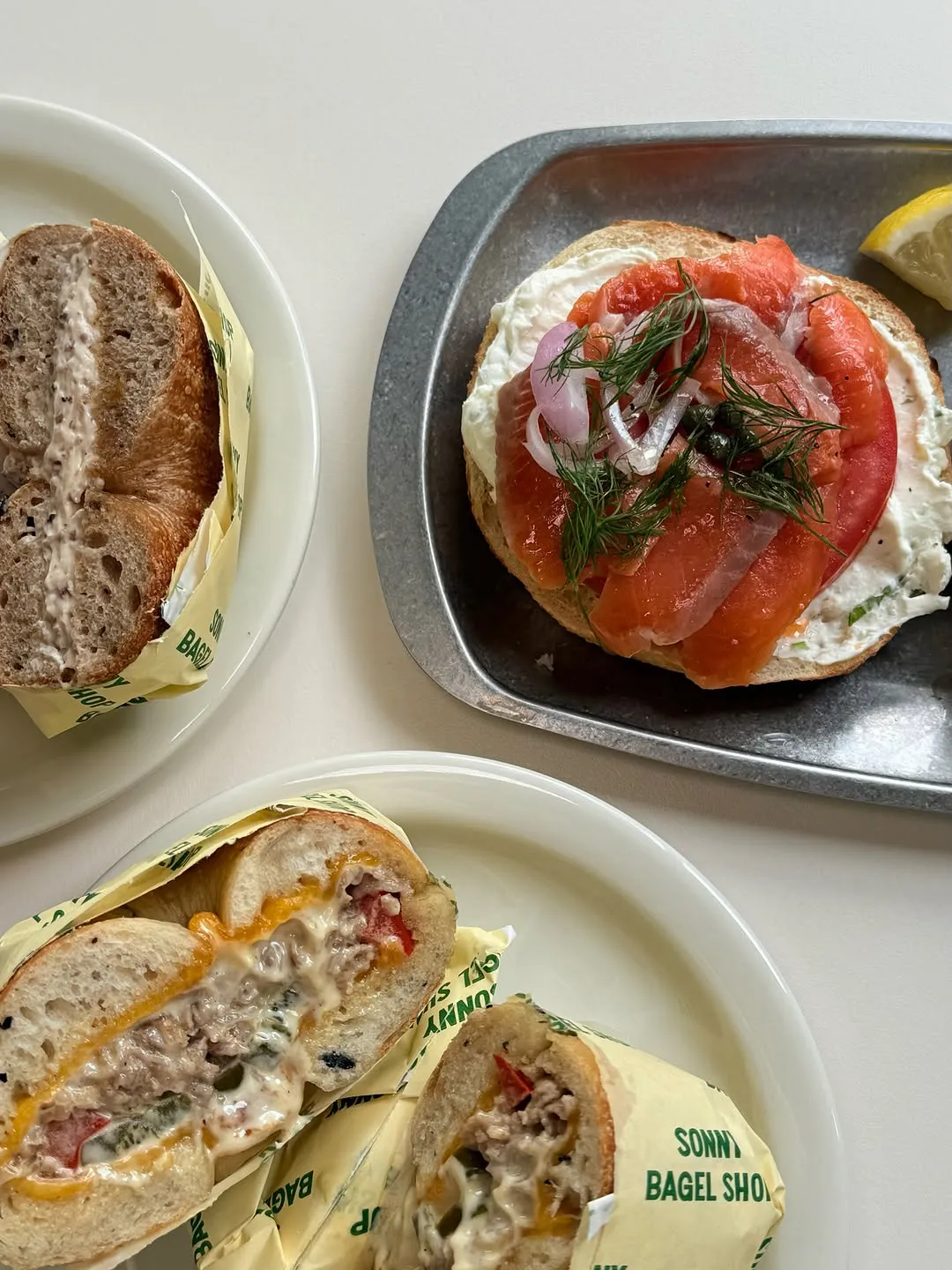 Salmon-topped bagel with cream cheese, garnished with vegetables and a lemon wedge.