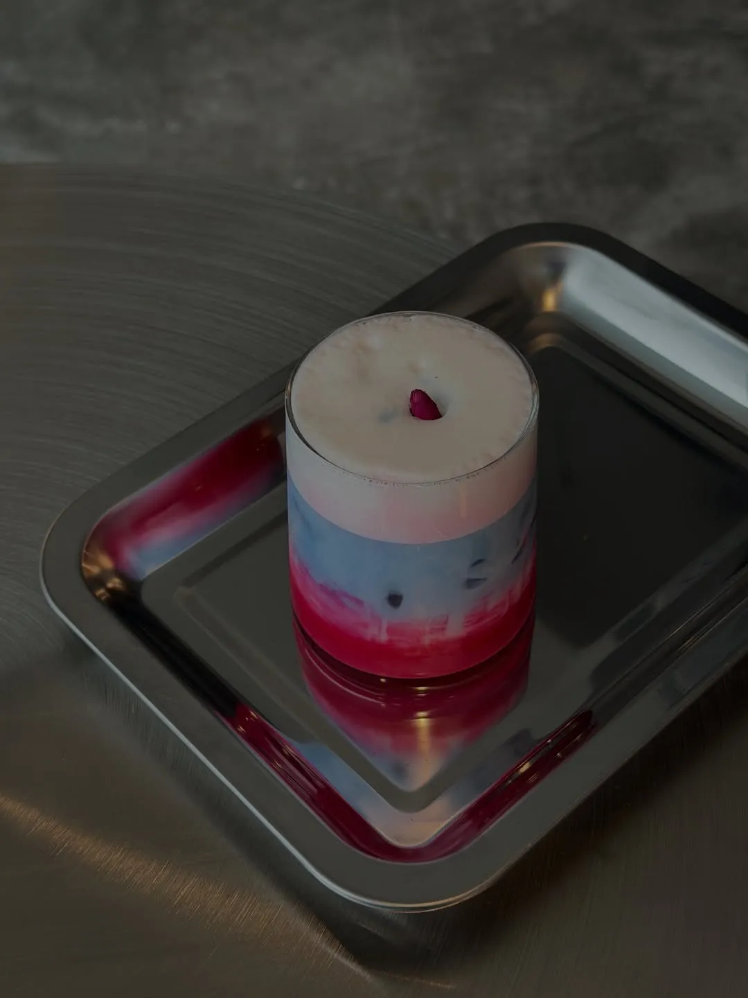 Beautiful layered drink with pink and purple hues on a stainless tray.