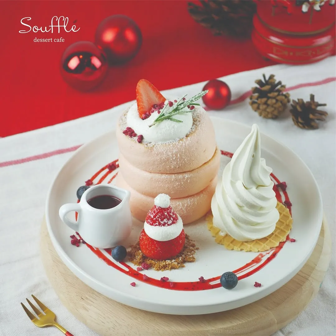 Strawberry souffle pancake topped with cream and festive decorations on a plate.