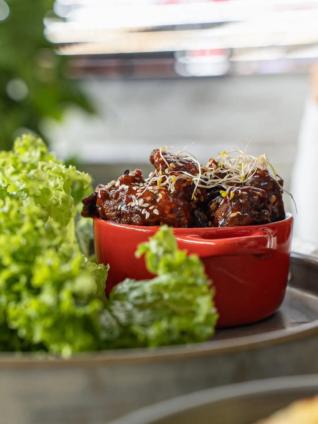 A vibrant bowl of sesame-coated chicken garnished with sprouts and lettuce.