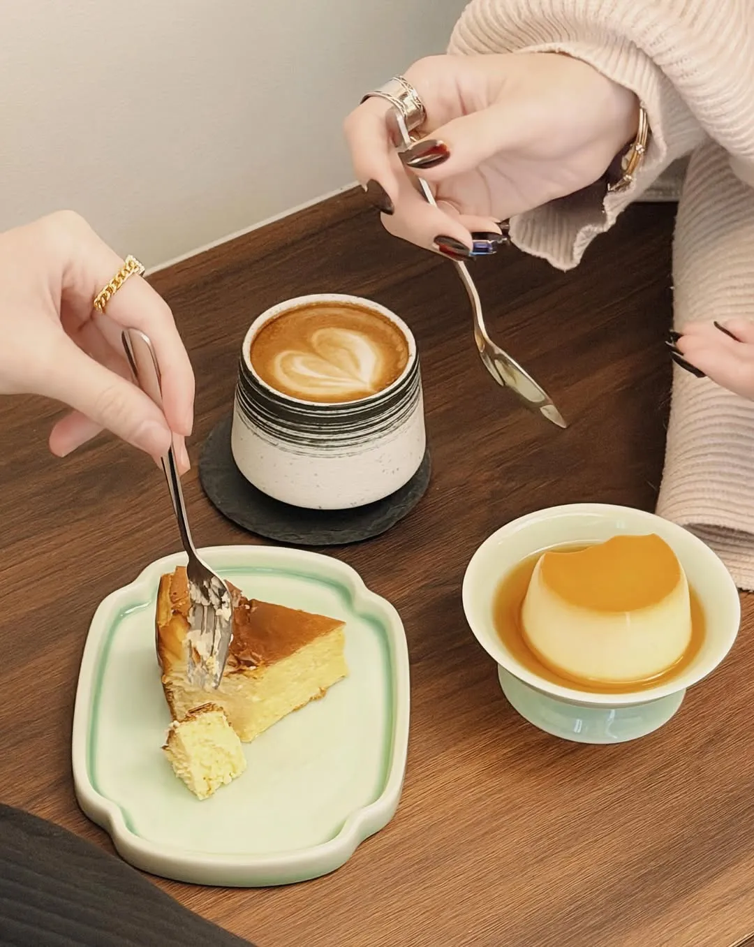 Two friends enjoying cheesecake, pudding, and coffee while sharing a table.