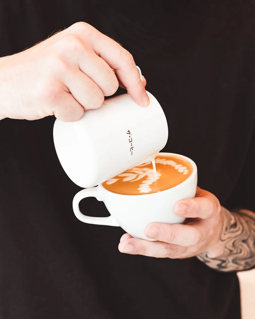 Barista pouring steamed milk into a latte, creating intricate latte art.