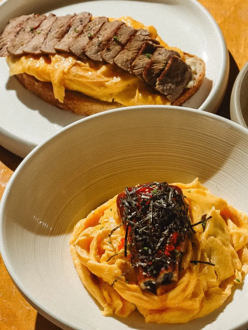 Hearty lunch of steak on bread and creamy pasta served in elegant dishes.