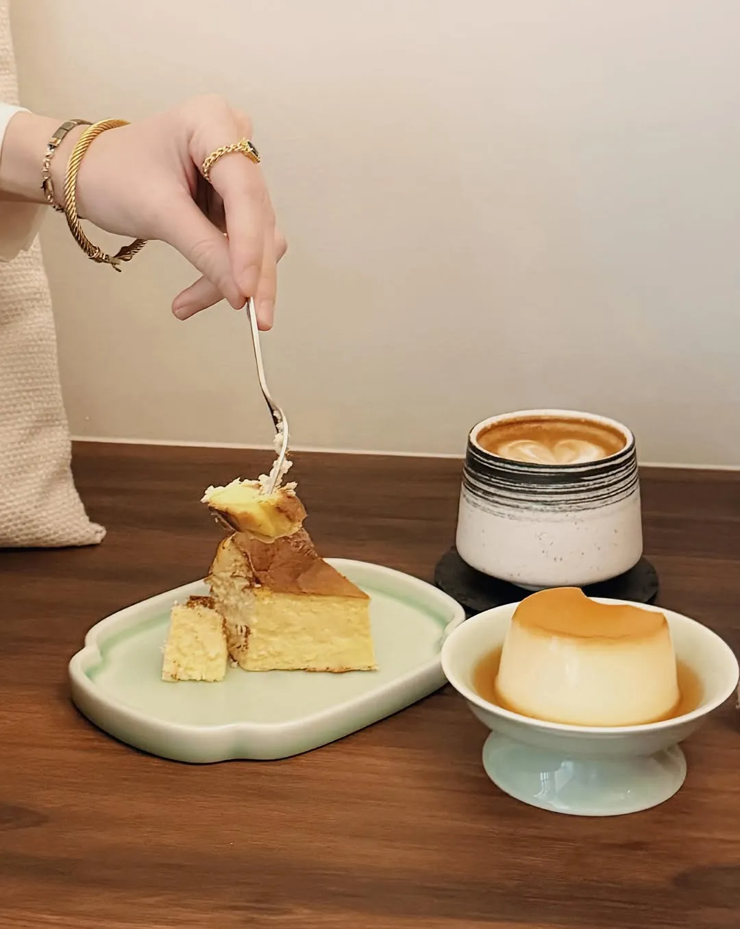 A piece of Basque cheesecake, pudding, and coffee on a wooden table.
