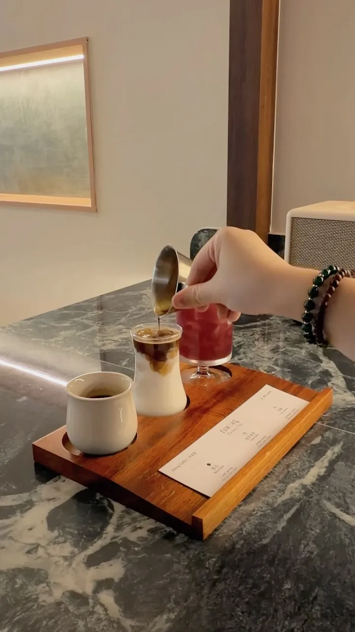 A trio of coffee cups with a hand stirring one cup on a marble table.