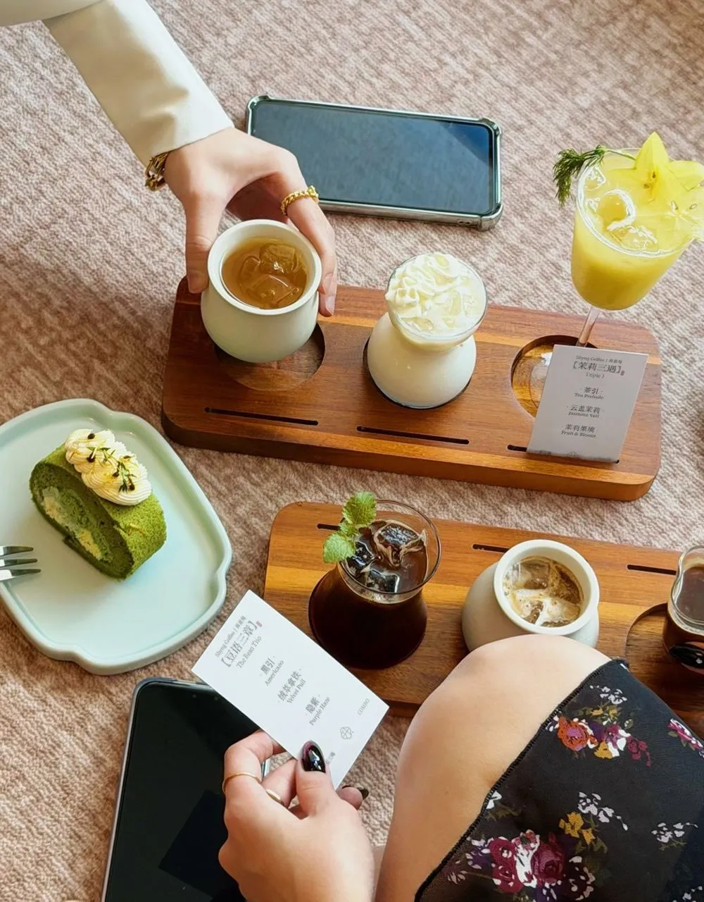 Multiple drinks arranged on a wooden platter with a dessert in the background.