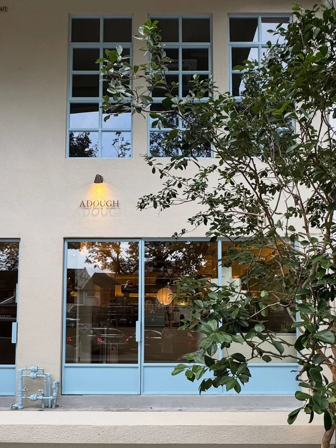 Charming exterior of ADOUGH Atelier with blue doors and greenery.