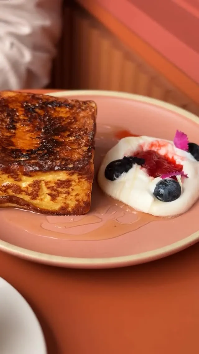 Freshly prepared French toast served with berries and cream on a pink plate.