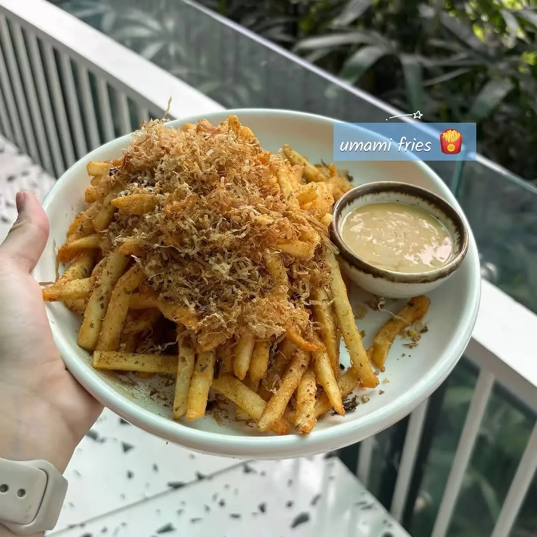 Plate of golden Umami Fries topped with savory seasoning and dip.