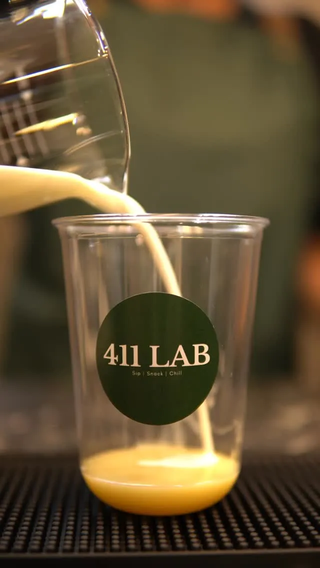 Pouring creamy milk into a transparent cup with 411 LAB branding.