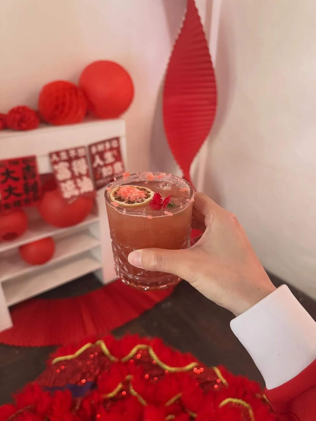 Hand holding a festive cocktail with garnishes in a vibrant setting.