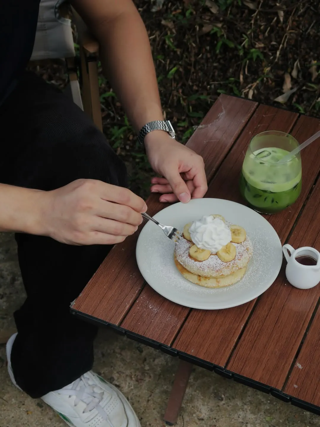 A hand reaching for fluffy banana pancakes topped with whipped cream and banana slices.