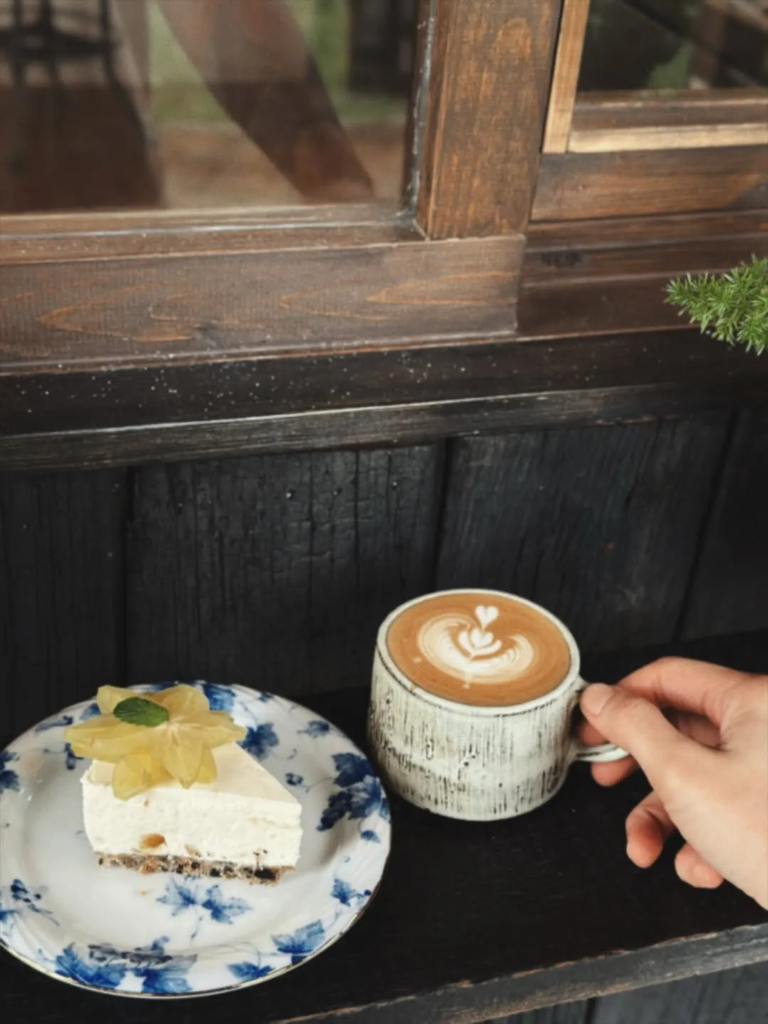 Cup of coffee with a slice of starfruit cheesecake on a floral plate.