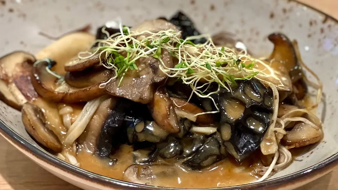 Gourmet mushroom dish with sprouts and rich sauce in a bowl.