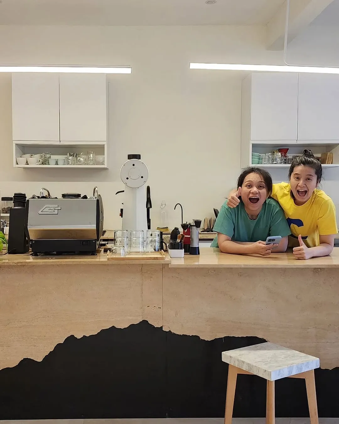 Baristas smiling joyfully at the counter with coffee equipment behind them.