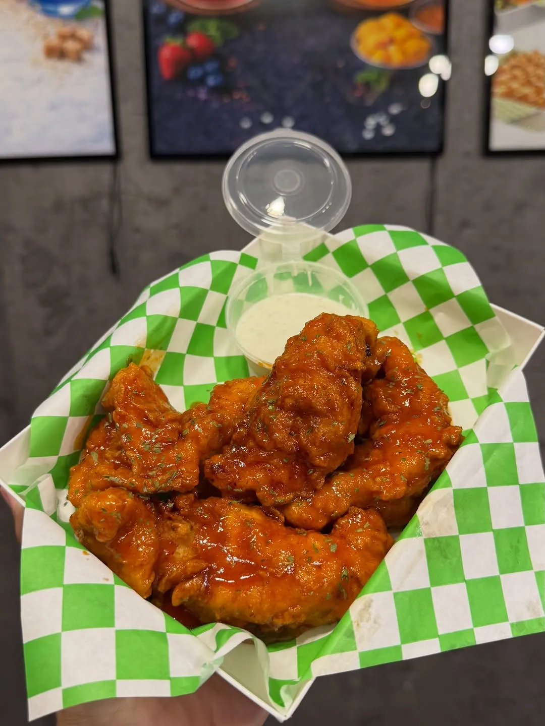 Basket of crispy chicken tenders drizzled in sauce with green checkered paper.