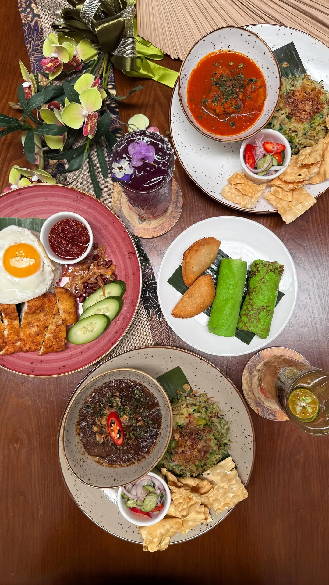 An array of dishes featuring rice, kuih, and colorful drinks on a table.