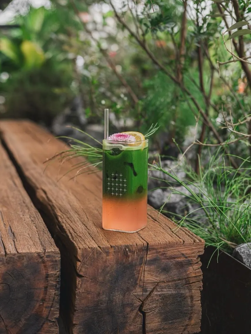 Colorful drink served on a wooden table surrounded by greenery.